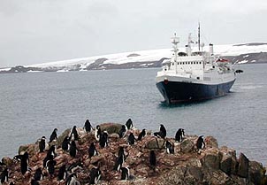A boat from Lindblad Expeditions approaches a penguin-encrusted rock. Copyright Cynthia Boal Janssens.